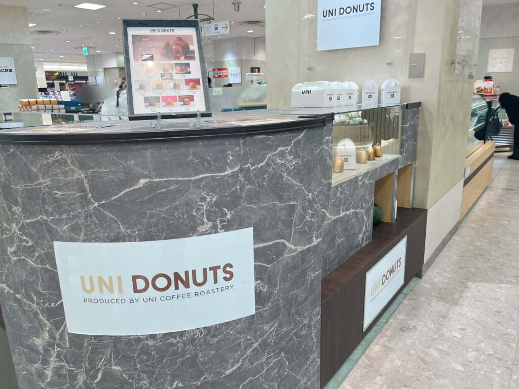店舗外観。デパ地下の一角に「ユニドーナツ」があり、ドーナツやカボチャがディスプレイされている。