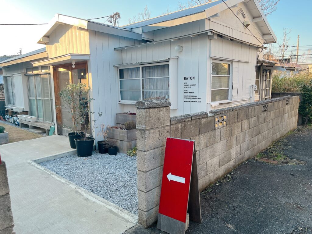白い平屋の古民家。お店の入り口には矢印が書かれた赤い看板がある