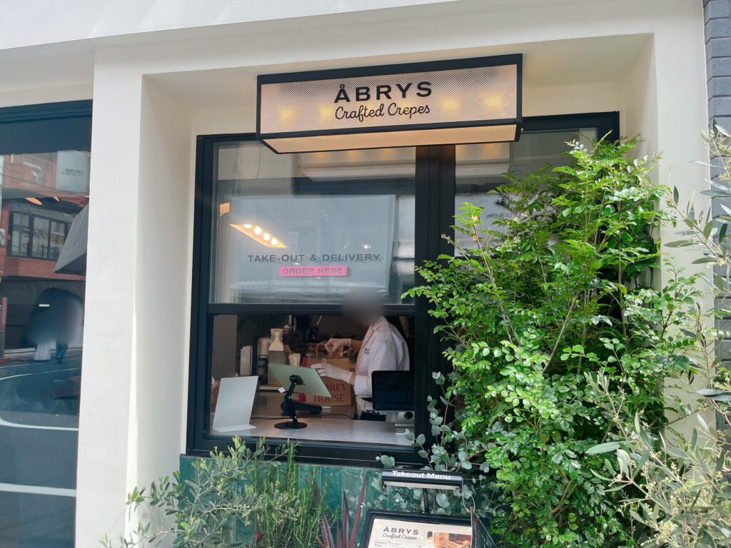 お店に併設されたテイクアウト注文口。白色の壁に黒枠のカウンター。手前には植物がありナチュラルな雰囲気。