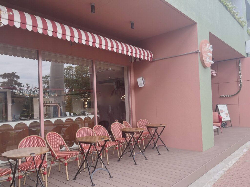 ピンクと黄緑色のおしゃれなカラーリングの壁面に、赤と白のインテリアが置かれた店舗外観。