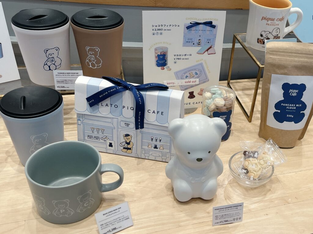 棚の上にテディベアの形をしたクッキー缶、マグカップ、タンブラーなどグッズが置かれている写真