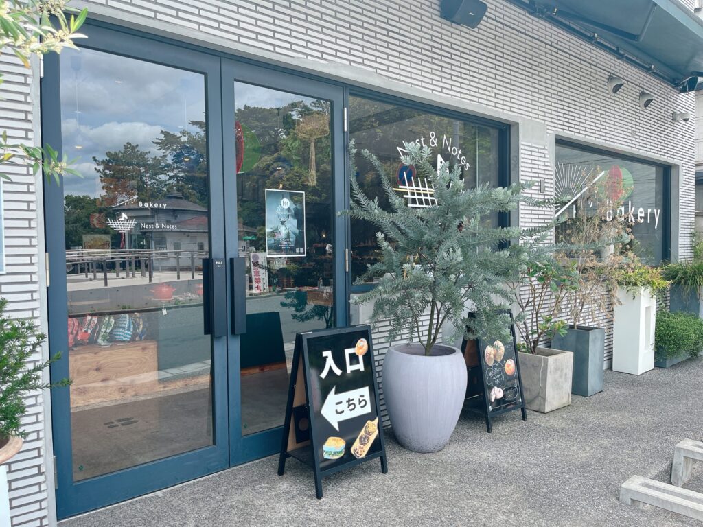 白いタイル張りの壁にガラス戸がついた店舗外観。植物がおしゃれに飾られている。