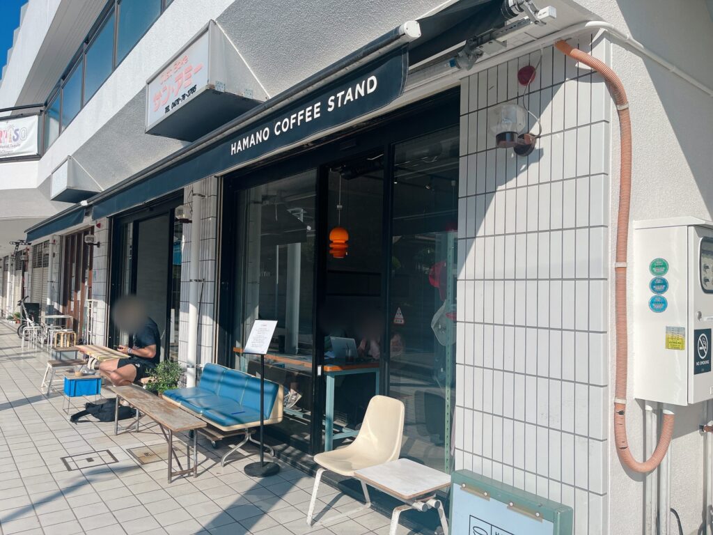 白いタイル張りの店舗外観。駅やバス停にあるような丸い椅子が置かれたテラス席がある。