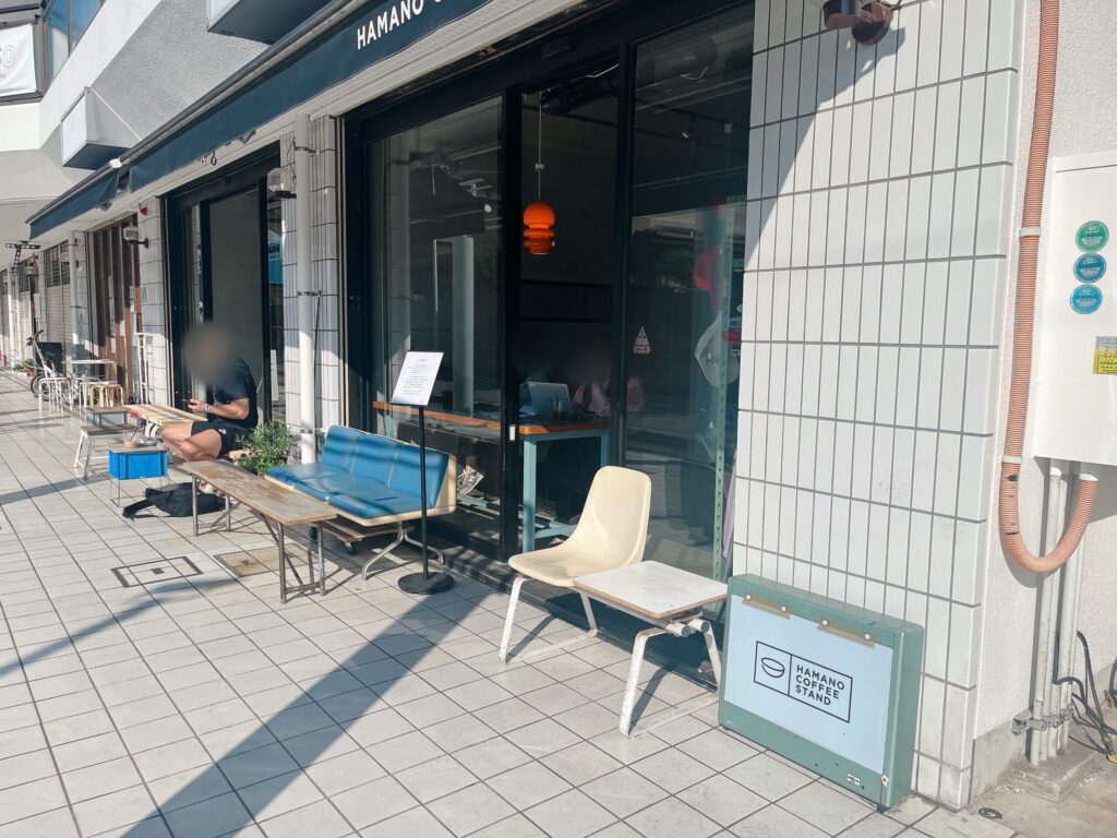 白いタイル張りの店舗外観。駅やバス停にあるような丸い椅子が置かれたテラス席がある。
