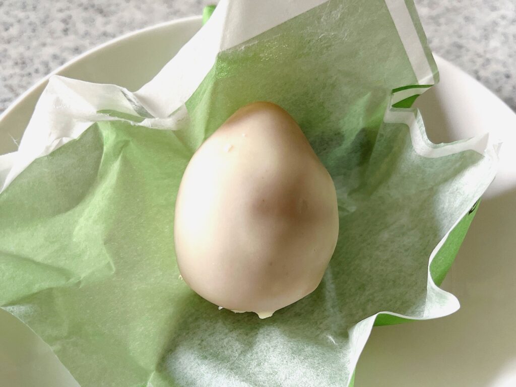 個包装の包装紙の上にホワイトチョココーティングされた卵型のお菓子が乗っている写真